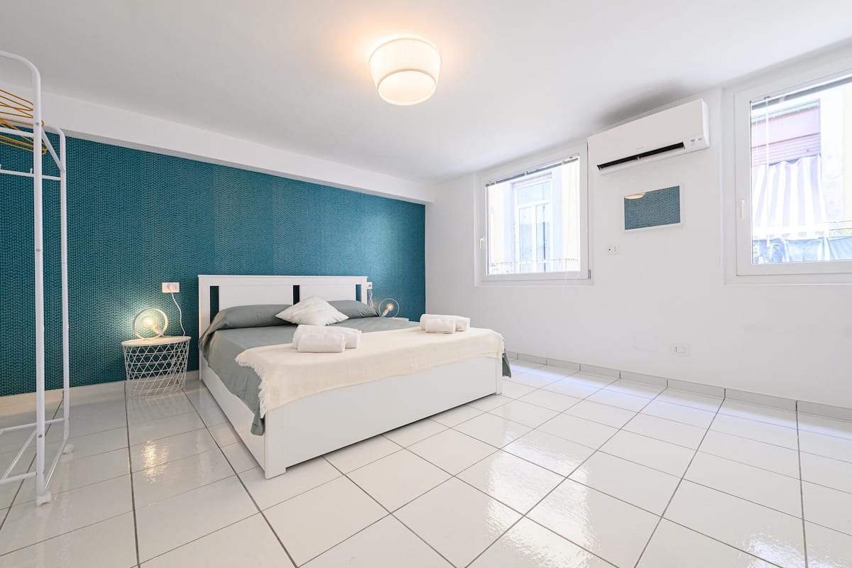 Une chambre moderne avec un lit blanc, un mur d’accent de couleur turquoise et une lucarne.