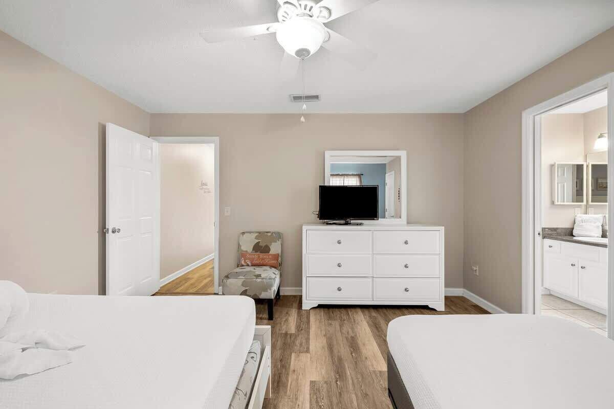 Un dormitorio con dos camas, un ventilador de techo, un televisor en una cómoda y una silla.