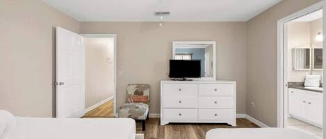 Un dormitorio con dos camas, un ventilador de techo, un televisor en una cómoda y una silla.