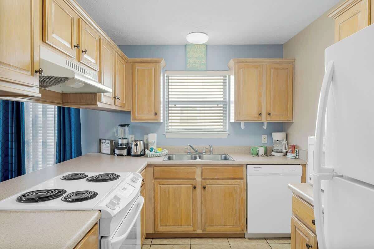 A compact kitchen with wooden cabinets, a white stove, a dishwasher, and a refrigerator.