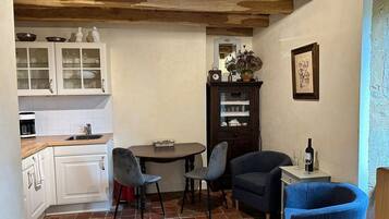 Een kleine keuken met witte kastjes, een koffiezetapparaat en een eethoek met twee stoelen en een tafeltje.