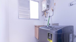 Ein Zimmer mit Waschmaschine, einem Fenster mit Jalousien und einem Wandheizkörper.