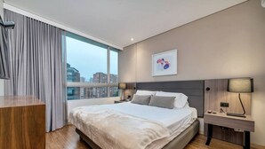 A modern hotel room with a large bed, a desk, and a view of the cityscape. - Luxury apt El Tesoro with AC and city view (Medellín)