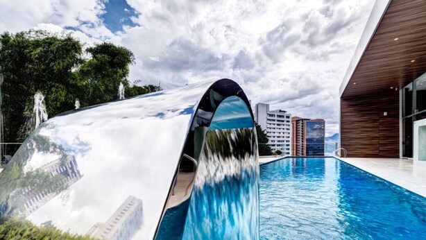 A modern building with a pool and a waterfall feature. - Luxury apt El Tesoro with AC and city view (Medellín)