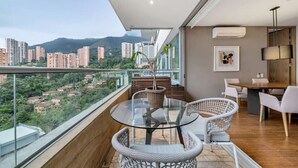 A balcony with a glass table and wicker chairs, overlooking a cityscape with high-rise buildings. - Luxury apt El Tesoro with AC and city view (Medellín)