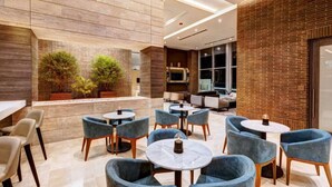 A modern indoor seating area with round tables and blue chairs, a brick wall, and a wooden panel wall. - Luxury apt El Tesoro with AC and city view (Medellín)