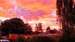 En solnedgång med en färgstark himmel, en liten byggnad och omgivande träd.