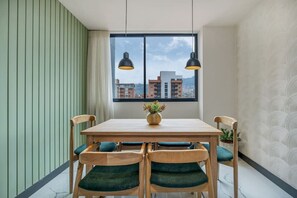 A dining area with a wooden table and chairs, a window with a city view, and pendant lights. - New Stylish 3BR apt AC in Laureles with fast Wifi (Medellín)