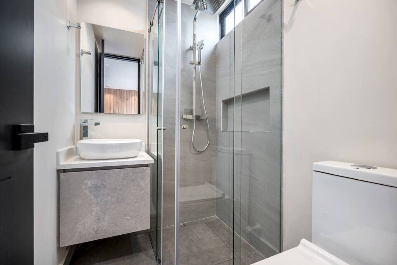 Ein modernes Badezimmer mit einer Duschkabine, einem weißen Waschbecken und einer Toilette.