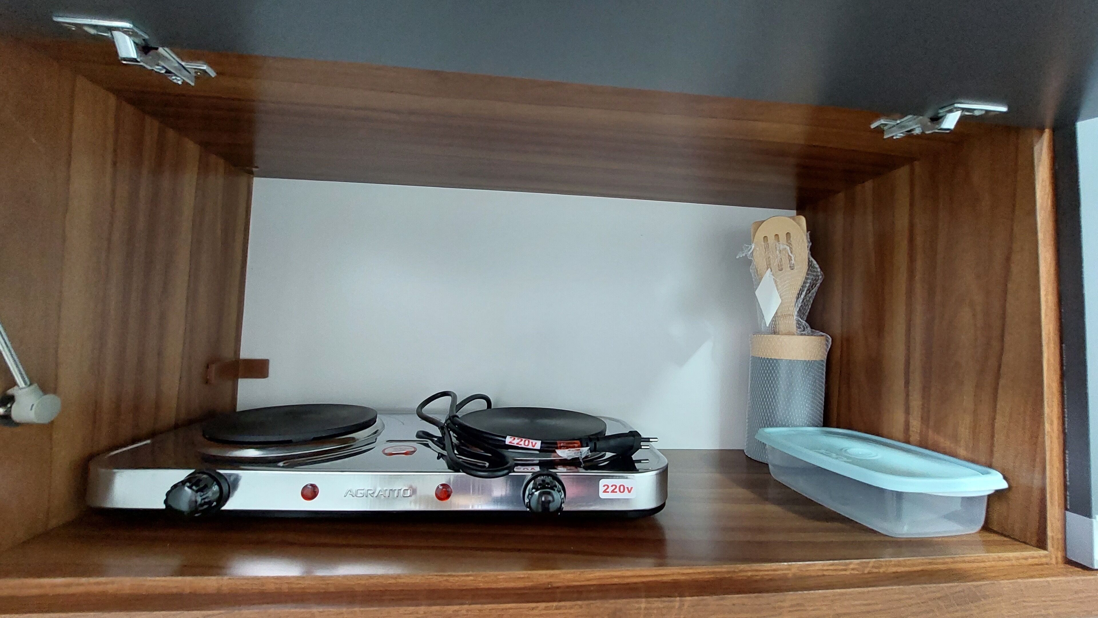 A compact kitchenette with a gas stove, a small sink, and a wooden utensil holder.