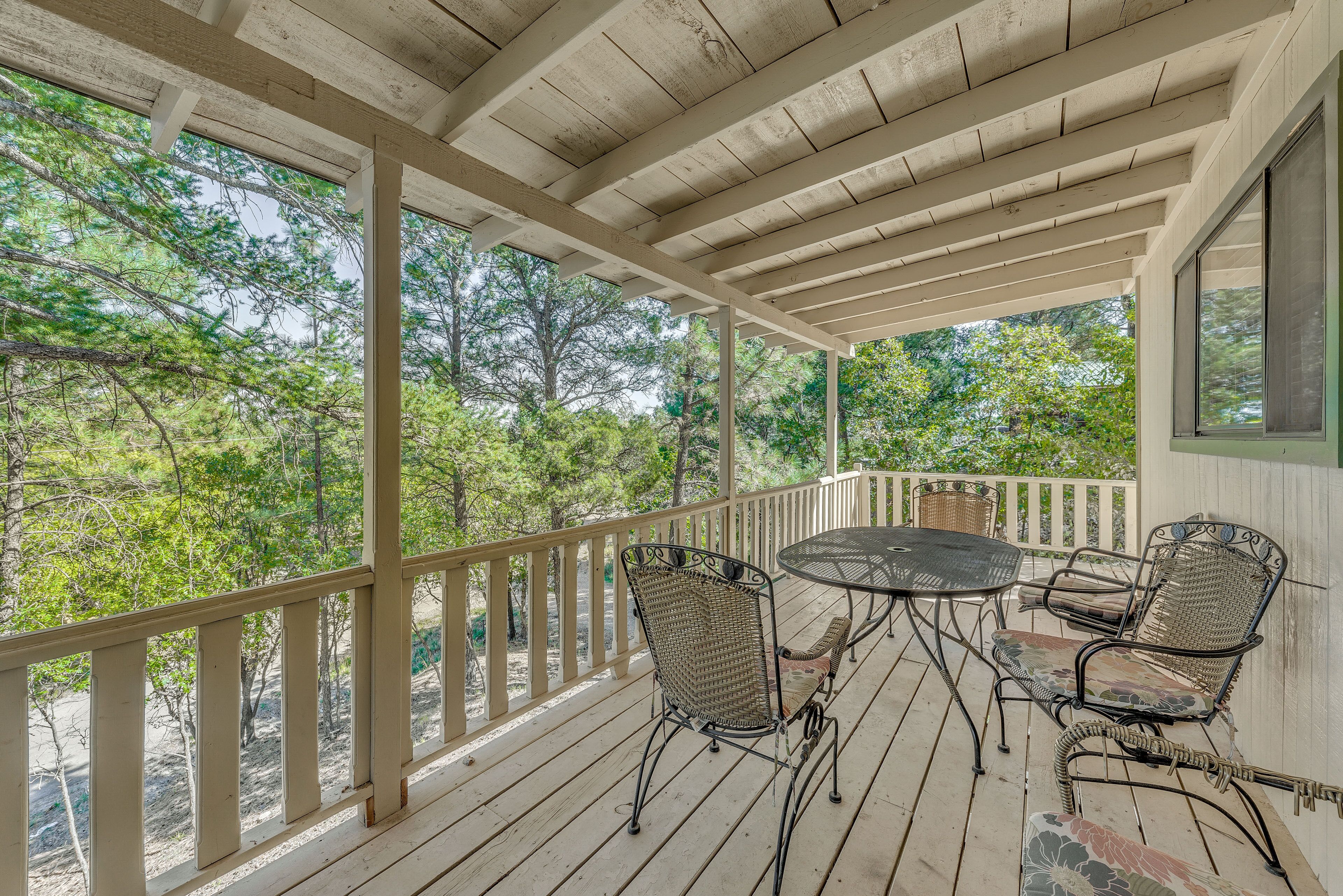 A covered outdoor area with a wooden deck, a table with chairs, and a view of trees.