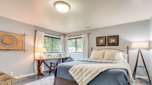 A bedroom with a bed, desk, and chair, a window with curtains, and a lamp.