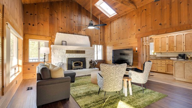 A cozy log cabin interior with a fireplace, a sofa, a dining table, and a TV in the living area. - Waterfront Mariposa Vacation Rental w/ Hot Tub (Mariposa)