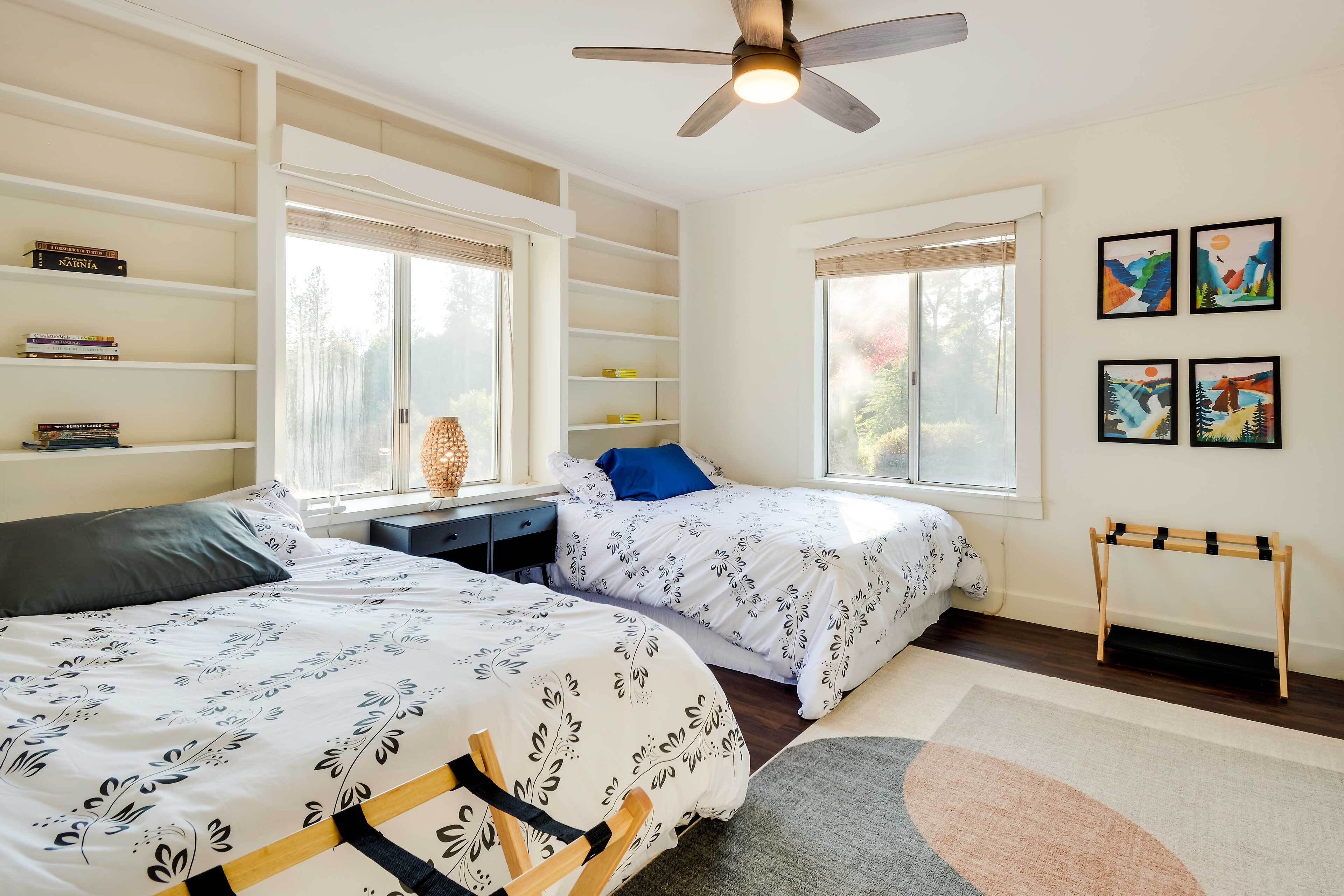 A bedroom with two beds, a ceiling fan, a bookshelf, and artwork on the wall.