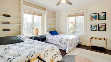 A bedroom with two beds, a ceiling fan, a bookshelf, and artwork on the wall.