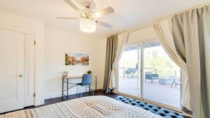 A bedroom with a large bed, a ceiling fan, a desk with a chair, and a view of the outdoors through a sliding glass door. - Waterfront Mariposa Vacation Rental w/ Hot Tub (Mariposa)