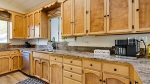 A kitchen with wooden cabinets, a stainless steel dishwasher, a coffee maker, and a sign that says "Butters Coffee." - Waterfront Mariposa Vacation Rental w/ Hot Tub (Mariposa)