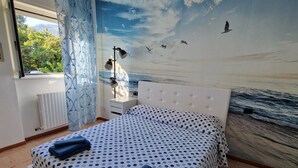Une chambre à coucher avec un lit, une fenêtre, un radiateur et une fresque murale représentant une scène de plage.