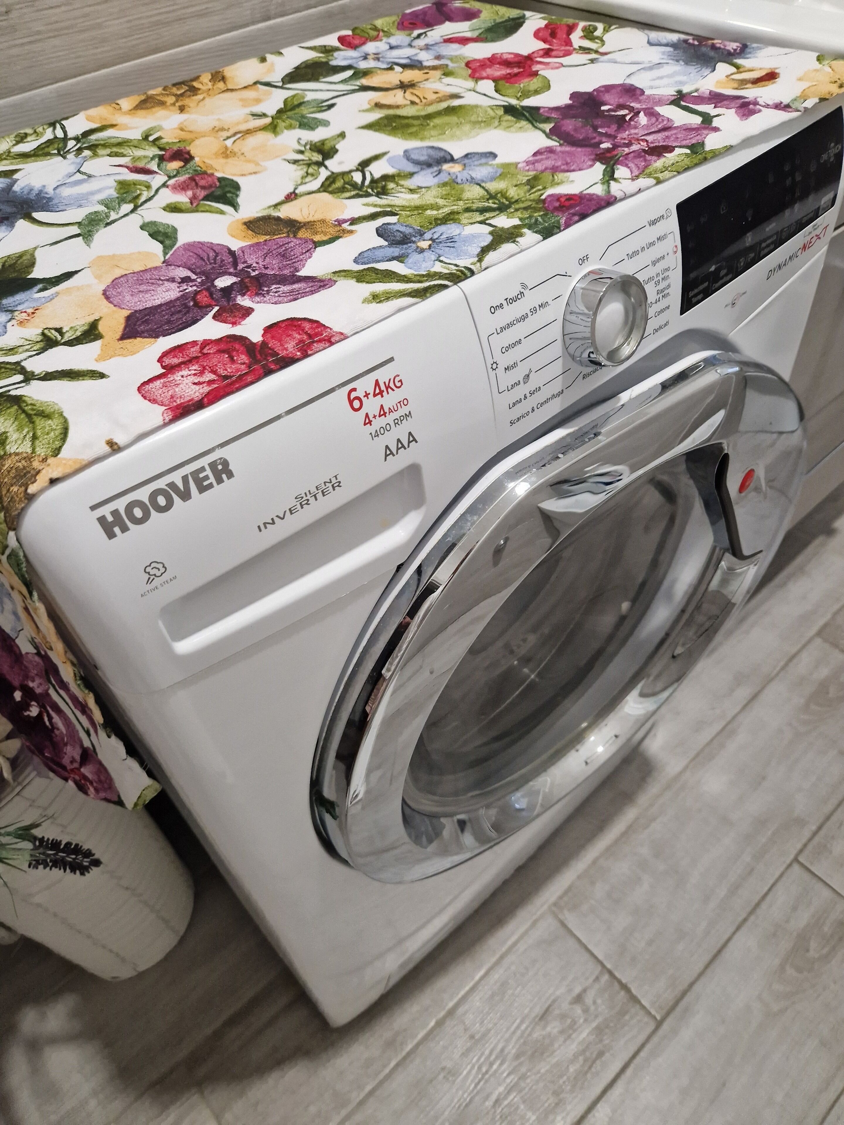 Een witte wasmachine met voorlader, voorzien van een bloemendecor, bedieningspaneel en een roestvrijstalen deur.