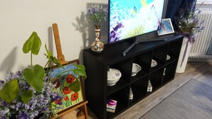 Un salon avec un téléviseur posé sur un meuble noir, un tableau sur un chevalet et un vase rempli de fleurs.