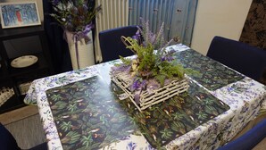 Une table à manger recouverte d’une nappe à motifs floraux, entourée de chaises et agrémentée d’un centre de table composé de fleurs et de feuillage.