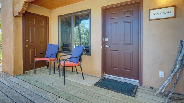 A wooden porch with two chairs, a brown door, and a sign reading "Ponderosa". - Pet-friendly Mountain Cabin in Taos County! (Amalia)