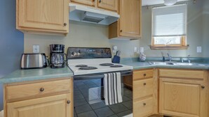 A kitchen with wooden cabinets, a stove, a toaster, and a coffee maker. - Pet-friendly Mountain Cabin in Taos County! (Amalia)