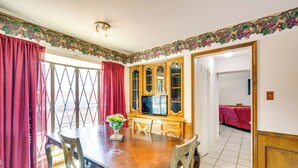 Ein Essbereich mit einem Holztisch, Stühlen und einem Fernseher. Rote Vorhänge und eine dekorative Bordüre zieren die Wände.