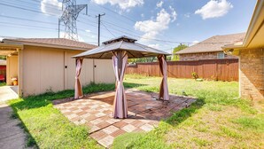 Ein Garten mit einer Terrasse, einer Pergola und einem Holzzaun.