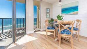 A balcony with a view of the ocean, a wooden dining table with chairs, and a hanging light fixture.