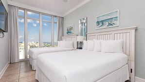A hotel room with two beds, large windows, a view of the city, and artwork on the walls.