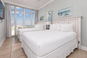 Een hotelkamer met twee bedden, grote ramen, uitzicht op de stad en kunst aan de muren.