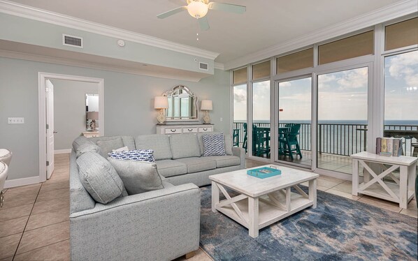 A spacious living room with a grey sofa, a coffee table, and a view of the ocean through large sliding doors.