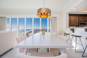 A modern dining area with a large table, white walls, and a view of the ocean. - Phoenix Gulf Towers 1701  Gulf-Front 4BR Condo (Orange Beach)