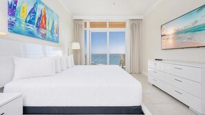 A spacious hotel room with a large bed, a ceiling fan, a TV, and a balcony with a view of the ocean. - Phoenix Gulf Towers 1701  Gulf-Front 4BR Condo (Orange Beach)