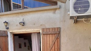 Une terrasse avec une table ronde et des chaises roses, une porte en bois et un pot de fleurs.