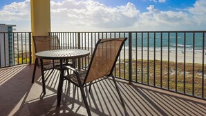A balcony with a table and chairs overlooking a beach.