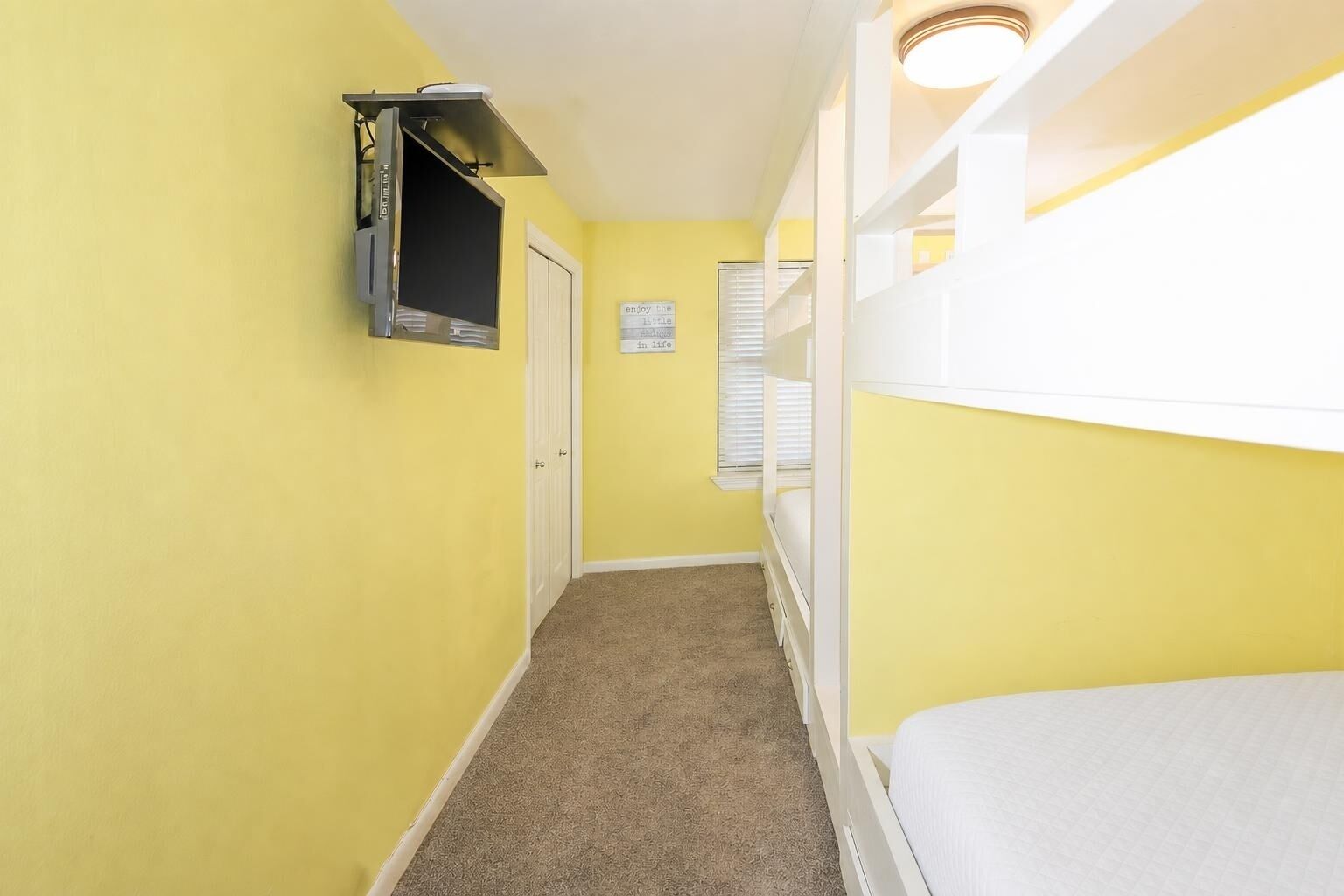 Un pasillo estrecho con una cama litera a la derecha, una puerta al fondo y un televisor montado en la pared.