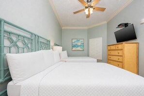 Une chambre avec deux lits, un ventilateur de plafond, une télévision, un tableau et une commode en bois.