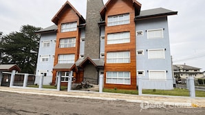 A multi-story building with a mix of brick and wooden facade, multiple windows, and a gated entrance. - Apartamento Morada do Sol Gramado (Gramado)