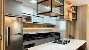 A modern kitchen with a stainless steel refrigerator, black countertops, a white marble island, and a built-in wine rack. - Apartamento Morada do Sol Gramado (Gramado)
