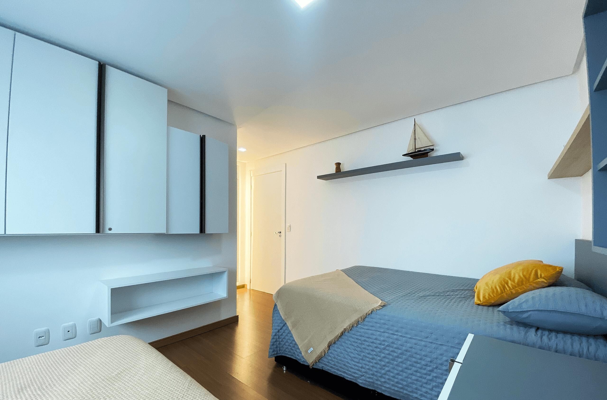 A modern bedroom with a bed, a wardrobe, a shelf with a model ship, and a door.