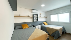 A modern hotel room with two beds, a built-in shelf, a small desk, and a window providing natural light. - Apartamento Morada do Sol Gramado (Gramado)