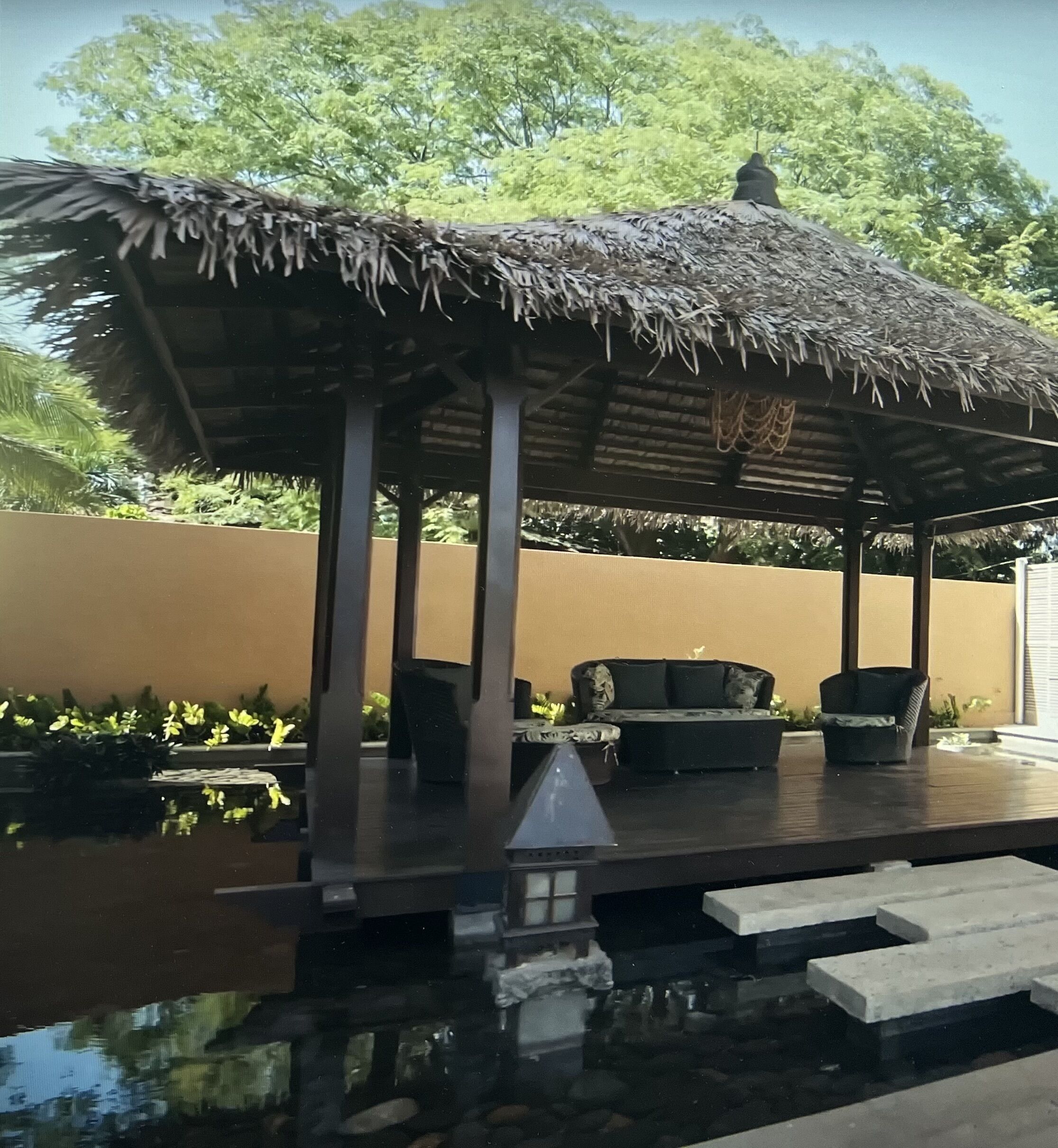 Un espacio de estar al aire libre cubierto con techo de paja, piscina y vistas a un paisaje verde y exuberante.