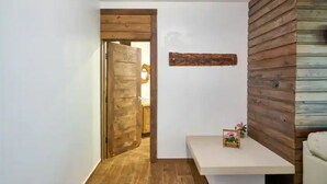 Een hal met een houten deur, een witte bank met een klein decoratief object, en een houten wandpaneel.