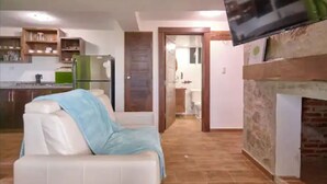 Un salon avec un canapé, un téléviseur à écran plat fixé au mur, une cheminée et un coin cuisine à l’arrière-plan.