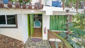 Une maison avec un chemin de pierres menant à une porte verte, une chaise bleue à l’intérieur et des plantes en pot sur le porche.