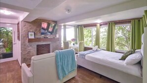Une chambre avec un lit, un canapé, un téléviseur fixé au mur et une cheminée.
