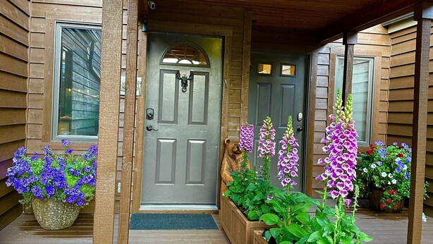 Una casa di legno con un portico, una porta grigia e fioriere.