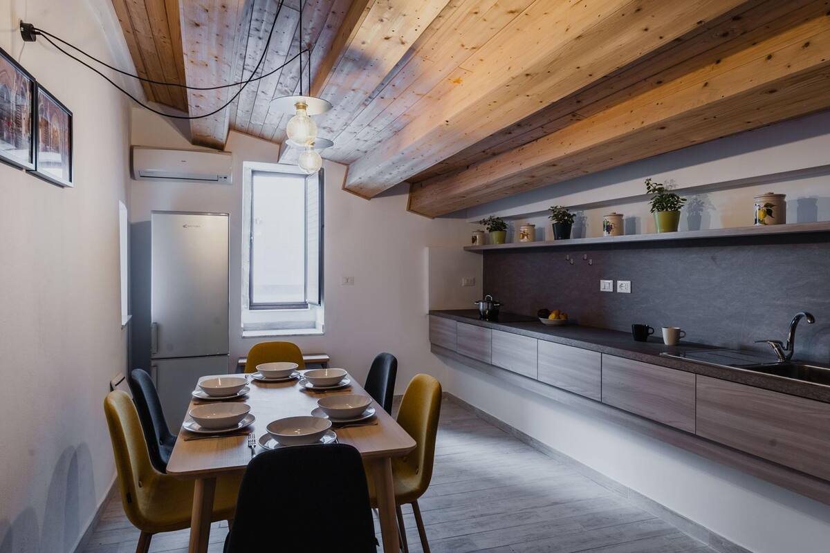 Eine moderne Küche mit Holzbalken, einem Essbereich mit Stühlen und einer eingebauten Regalfläche mit Pflanzen.